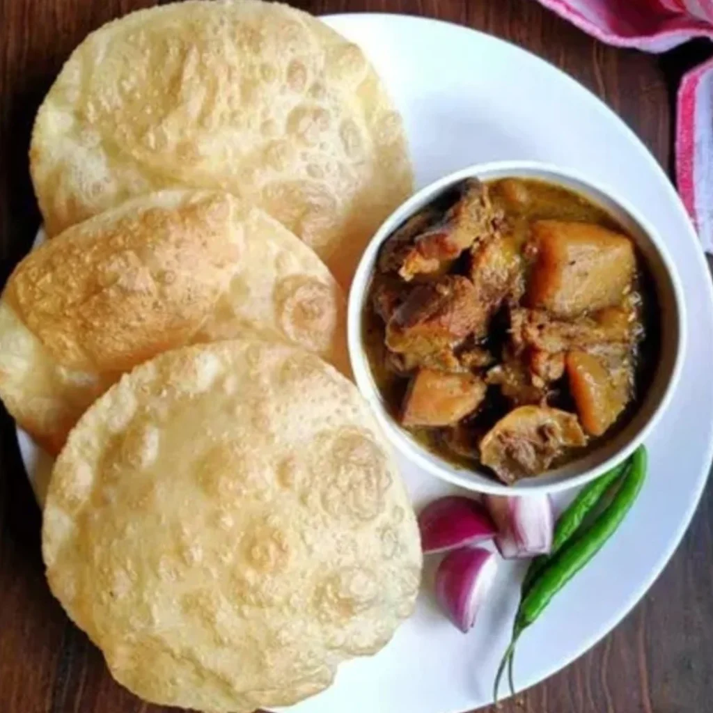 "Traditional Bengali luchi served with mutton curry, garnished with red onions and green chilies on a white plate"