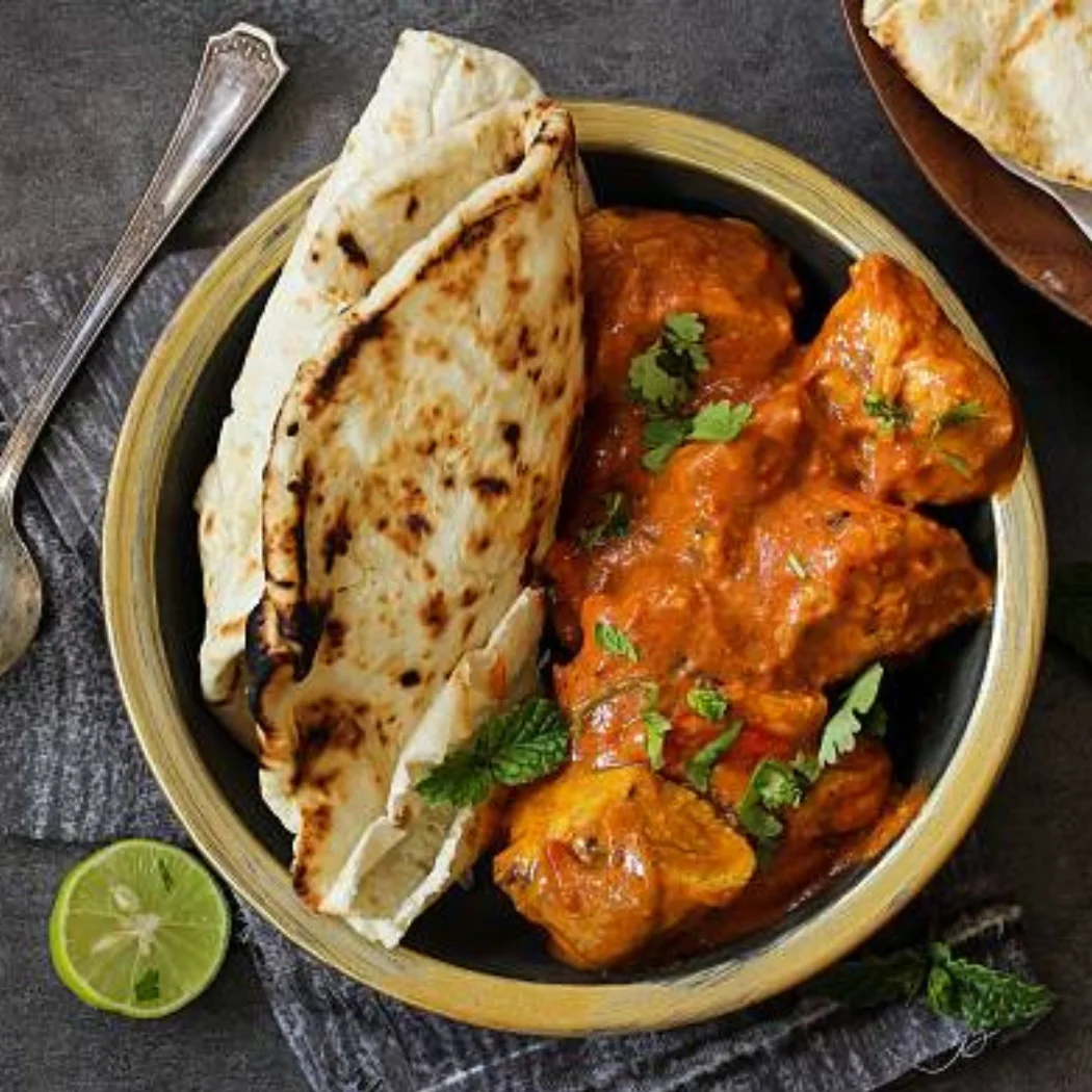 "Butter chicken curry with naan bread and lime garnish served in a ceramic bowl"