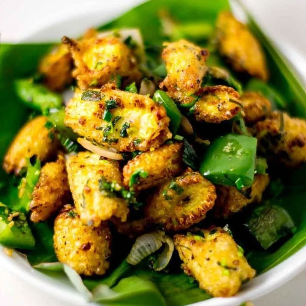 "Salt and pepper crispy honey garlic chicken bites with green bell peppers and fresh herbs served on banana leaf"