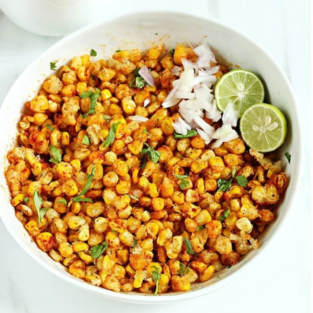 "Spicy Mexican street corn kernels (Esquites) garnished with fresh cilantro, diced onions, and lime wedges in a white bowl"