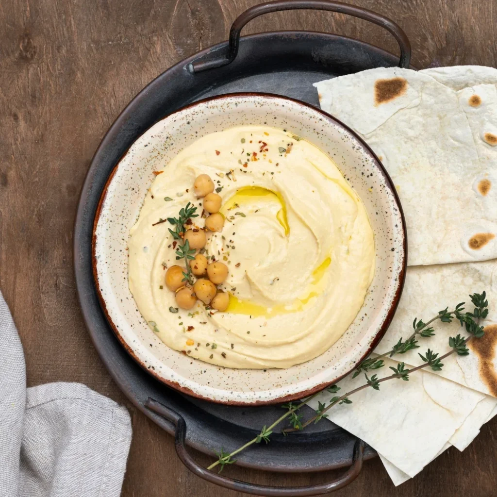 "Creamy homemade hummus served with chickpeas, olive oil, herbs and flatbread"