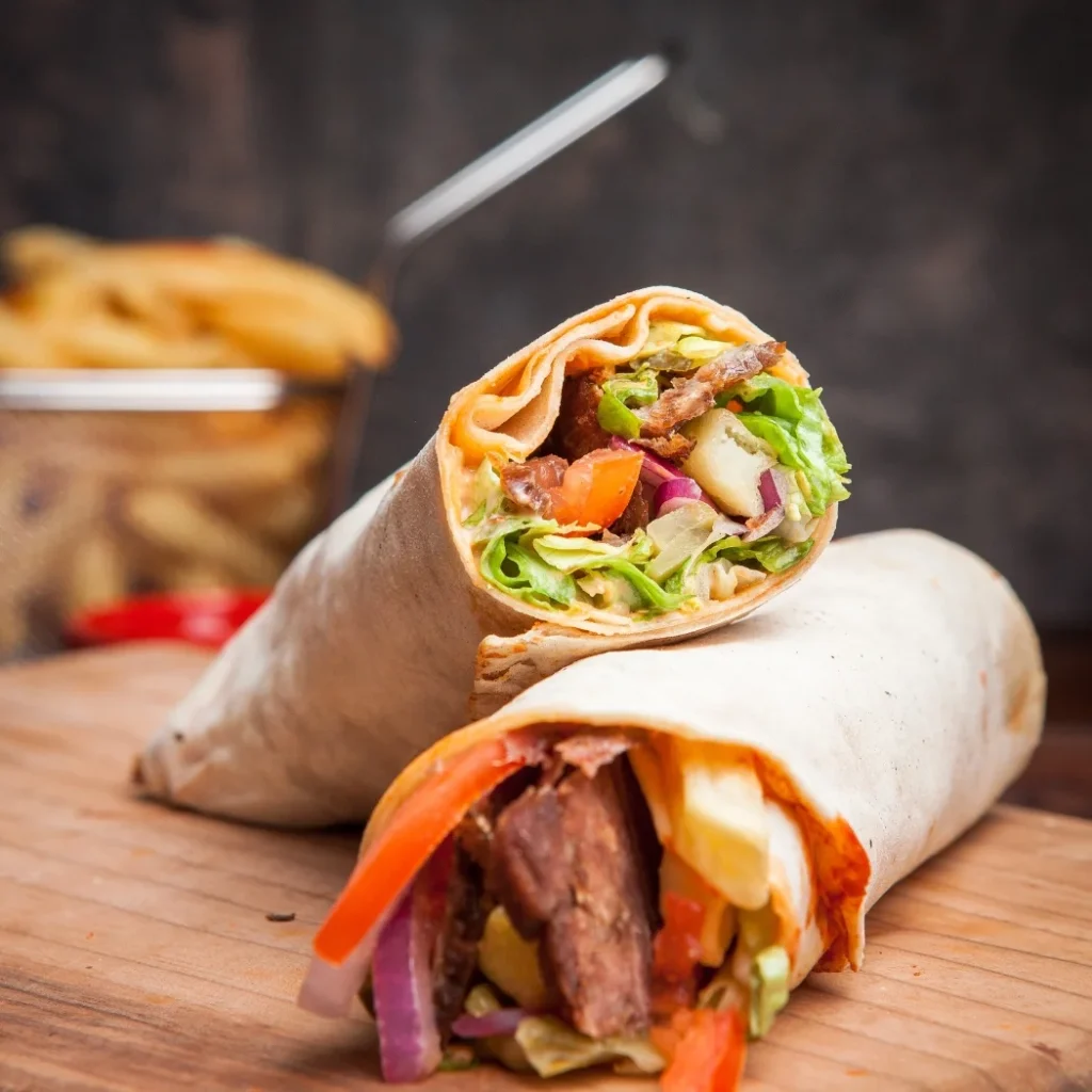 "Grilled steak wrap with fresh vegetables and bacon served on wooden cutting board"