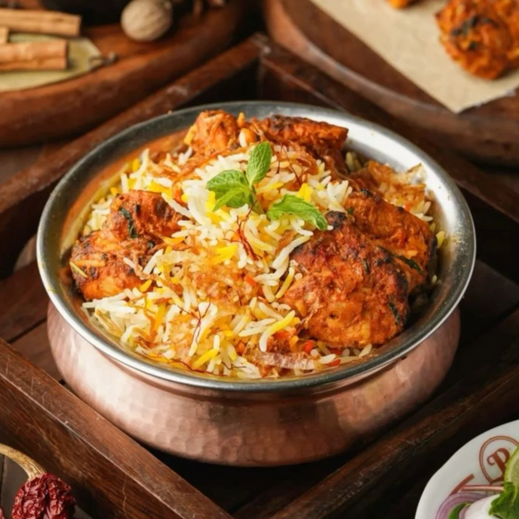 "Tandoori chicken biryani served in traditional copper handi with saffron rice, mint garnish, and aromatic Indian spices"