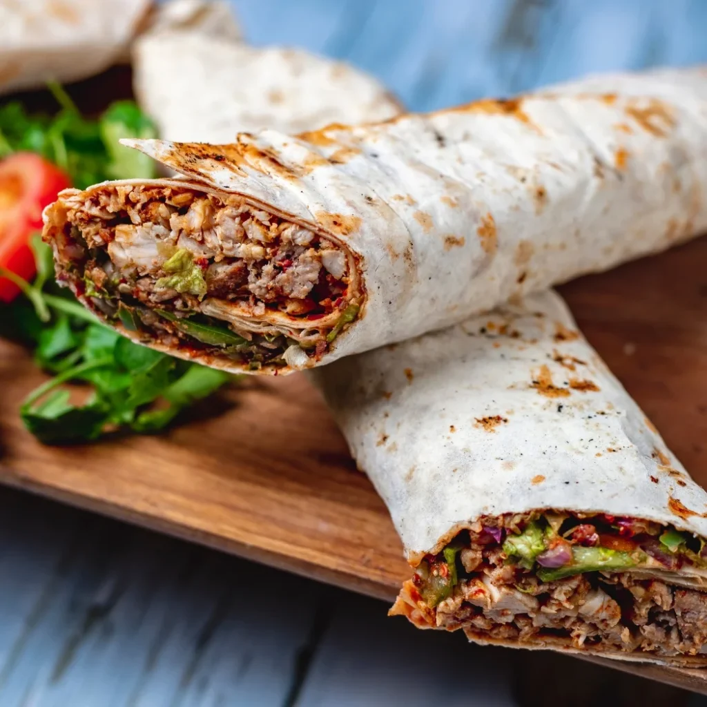 "Grilled chicken shawarma wrap with fresh vegetables and sauce on wooden cutting board"