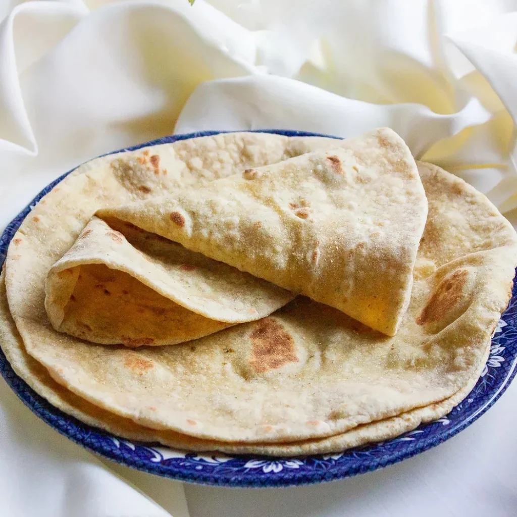 "Homemade soft flour tortillas stacked on blue and white decorative plate against white background"