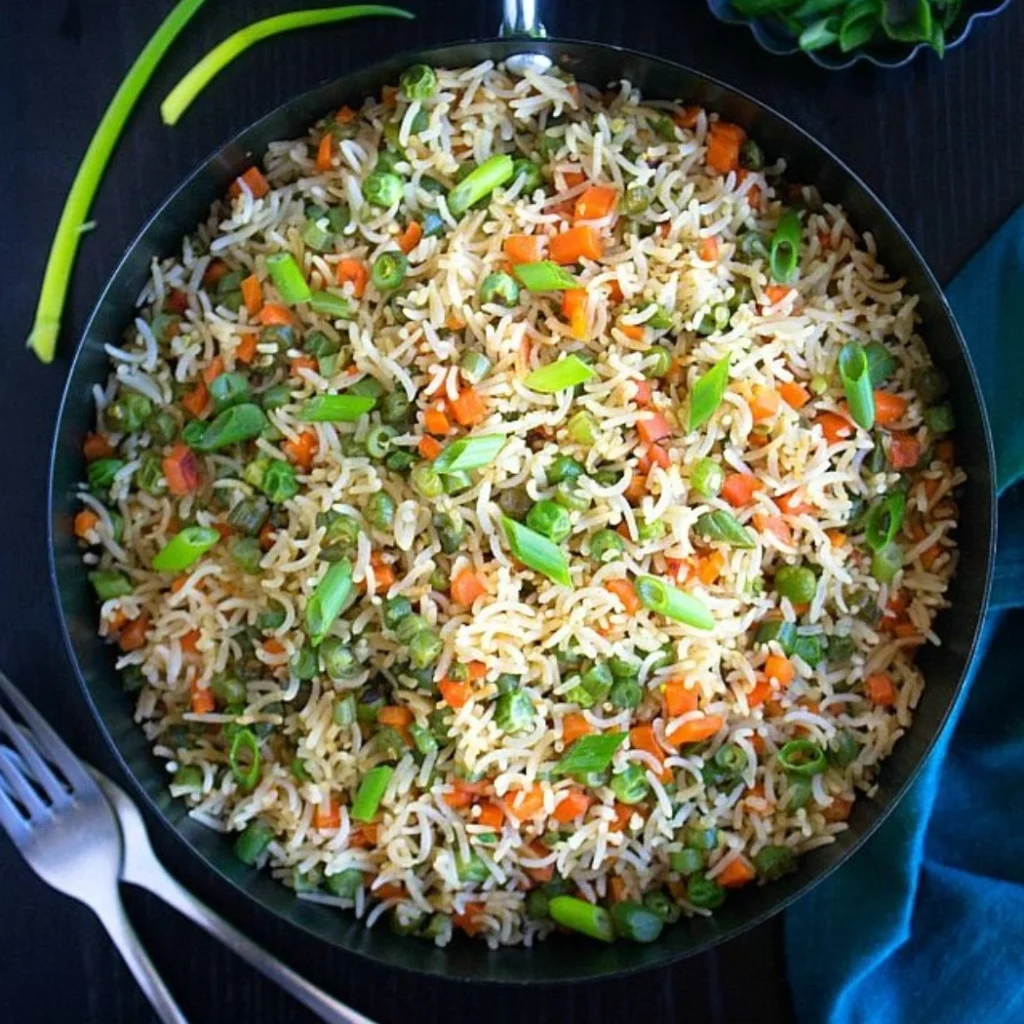 "Homemade vegetable fried rice with carrots, green onions, and aromatic basmati rice served in a black pan"