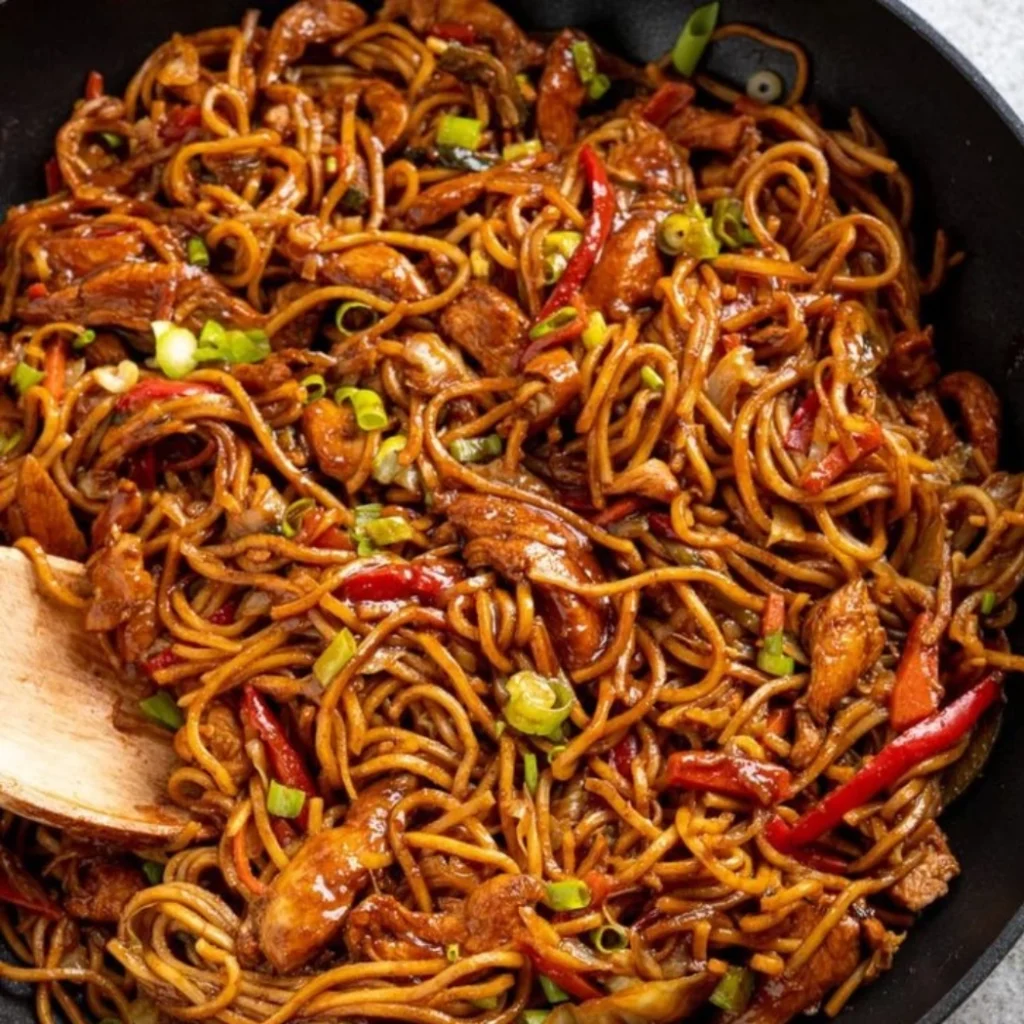 "Spicy chicken lo mein noodles with colorful bell peppers and green onions in a black skillet"