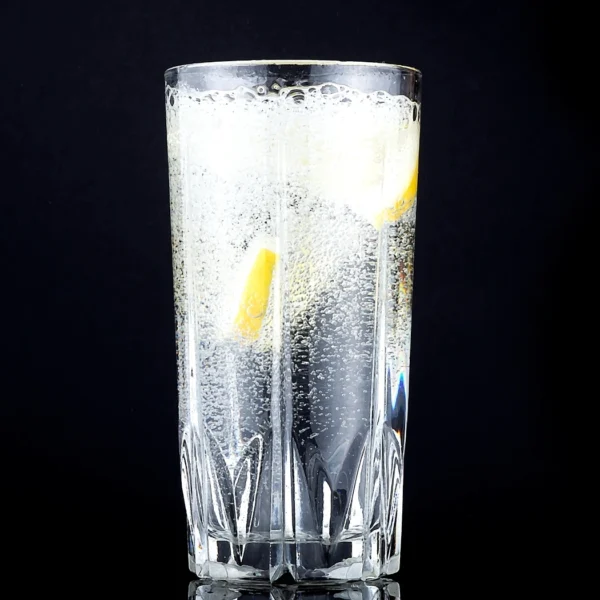 "Refreshing glass of sparkling water with lemon slices in a crystal highball glass against black background"