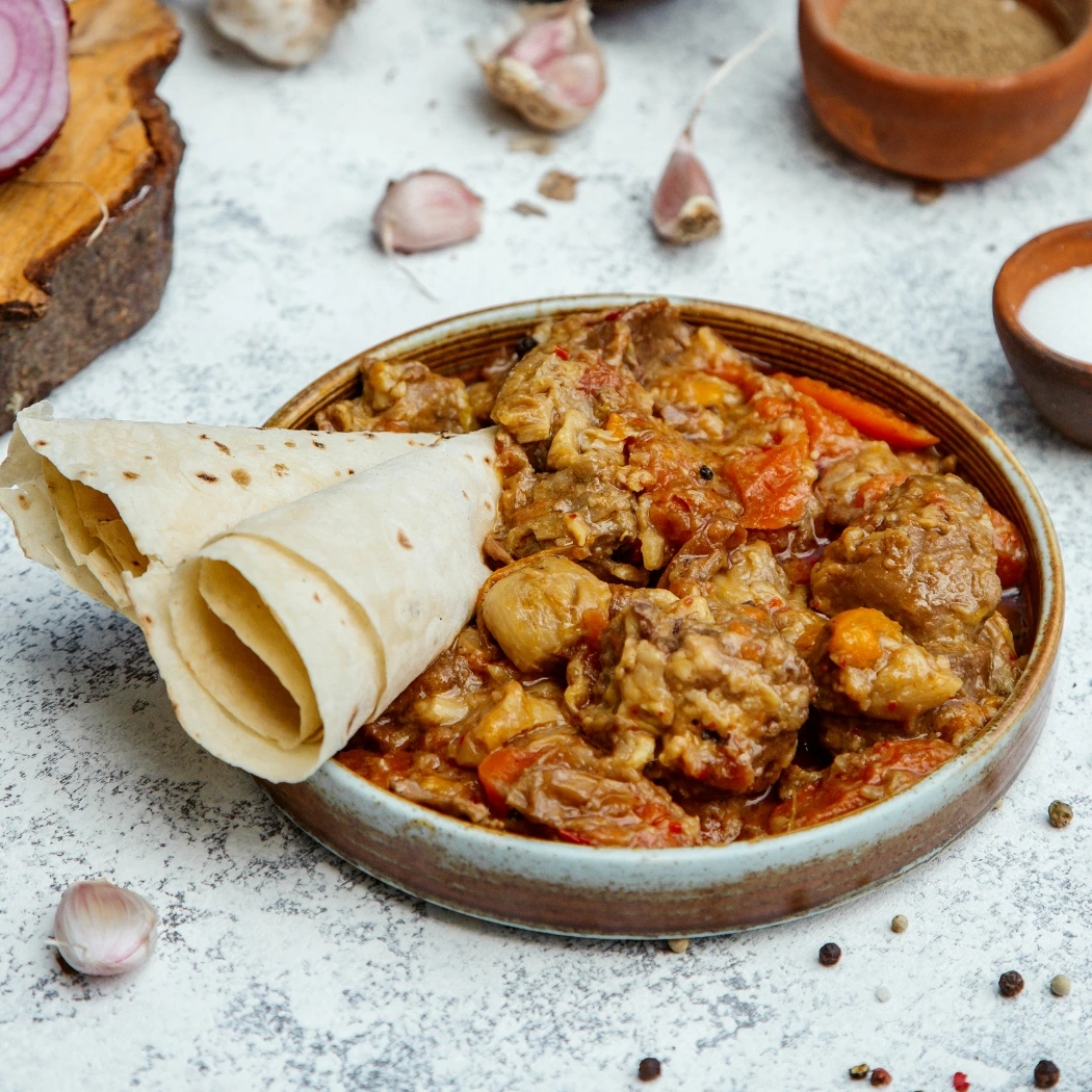 "Homemade chicken curry served with soft rotis, garnished with garlic and spices on rustic ceramic plate"