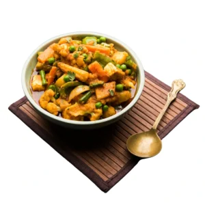 "Mixed vegetable curry with potatoes, carrots, green peas, and bell peppers in a white bowl with traditional brass spoon"
