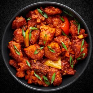 "Spicy Korean Gochujang Chicken garnished with green onions and bell peppers in a black bowl"